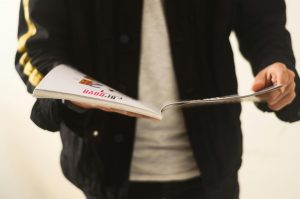 Close-up of a man in a casual jacket flipping through a magazine.