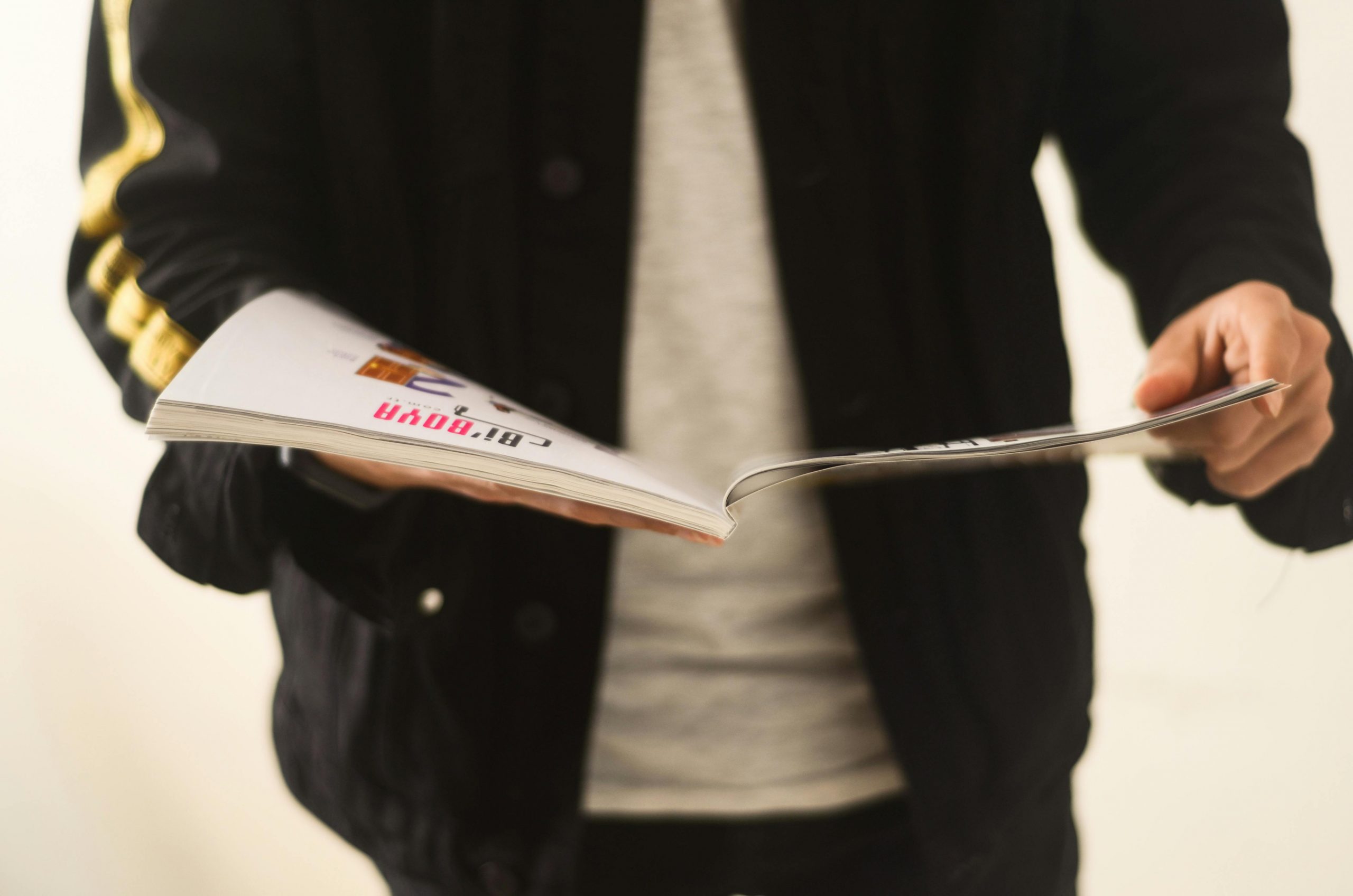 Close-up of a man in a casual jacket flipping through a magazine.